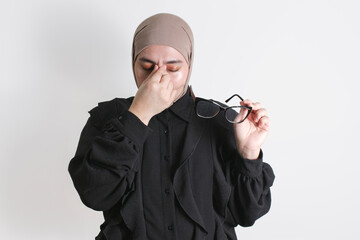 Tired Woman in hijab rubbing her eyes and holding glasses, showing signs of fatigue and exhaustion...