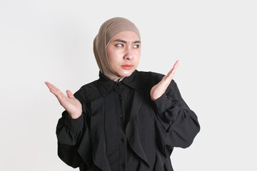 Confused Woman in hijab raising hands and frowning, showing uncertain or clueless expression on...