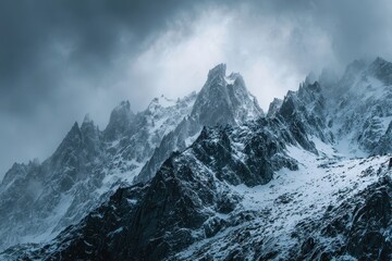 Dramatic landscape shot of rugged mountain peaks covered in snow beneath cloudy sky