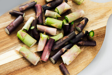 The hard part of an asparagus stalk that is not cooked arranged on a wooden cutting board for...