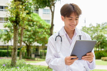 Young healthcare worker wearing lab coat sitting in park using tablet computer