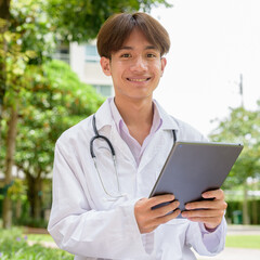 Young healthcare worker wearing lab coat sitting in park using tablet computer
