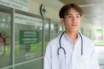 Young healthcare worker wearing lab coat in front of medical clinic thinking