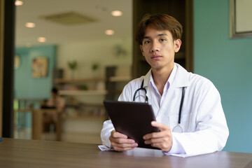 Young healthcare worker wearing lab coat sitting inside clinic library