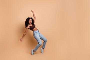 Joyful young woman dancing playfully in casual stylish attire on a beige background, expressing fun and cheerful vibes
