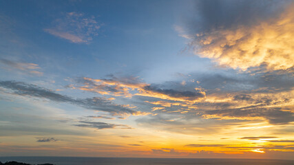 Fototapeta premium A breathtaking sunset paints the sky in vivid hues of orange and blue over a coastal town, with lush green hills framing the scene. A distant hilltop structure adds a serene tranquil landscape.