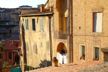 Warm evening light casts shadows on traditional Tuscan buildings with shutters, balconies, and...