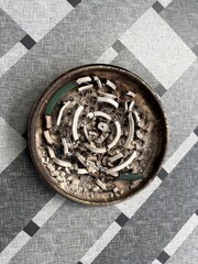 Top-down view of a used mosquito coil in a metal ashtray, showing broken ash remnants in a spiral pattern.