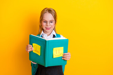 Young girl in school uniform holding a book, smiling happily on a yellow background, representing...