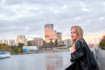 Fototapeta premium A woman stands on a bridge overlooking a river. The sky is cloudy and the sun is setting
