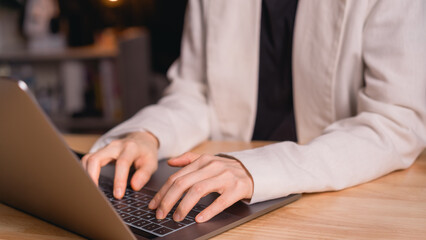 Businesswoman wearing light blazer typing on laptop at wooden desk in office illustrating work...