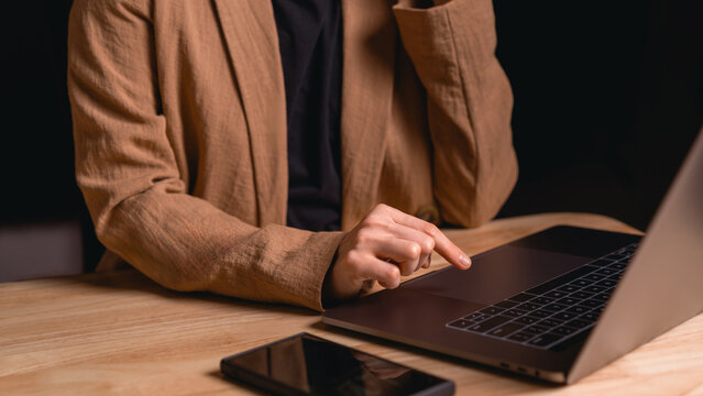 Businesswoman touching laptop trackpad at wooden desk with smartphone nearby representing modern remote work productivity and technology use