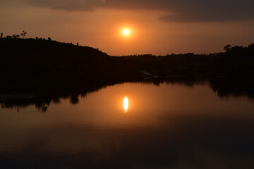 Golden sun setting over a calm waters of a river in Jowai, Meghalaya, with reflection.