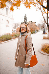 Smiling mature woman wearing eye glasses and autumn jacket over yellow leaves outdoors. Fall...