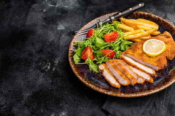 Roast viennese schnitzel steak, breaded meat with salad and french fry on a plate. black...