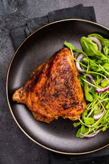 Roasted chicken thigh with salad on a plate, poultry meat. black background. top view