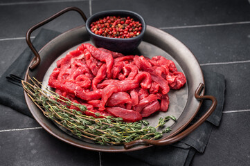 Beef sliced meat, raw veal strips for cooking beef stroganoff on a steel tray. black background. top view