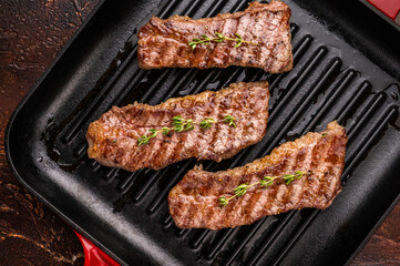 Grilled Tri tip steaks, marbled beef meat on pan with herbs. brown background. top view