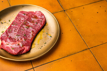 Marinated with olive oil and herbs Raw top sirloin or rump beef steak. orange background. top view