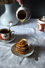 Pancakes with walnuts and honey on rustic breakfast table. Syrup being poured from ceramic jug