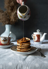 Pancakes with walnuts and honey on rustic breakfast table. Syrup being poured from ceramic jug