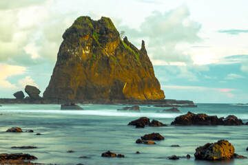 A mystical long exposure shot of a rocky coastline at sunset, with a waterfall-like rock formation...