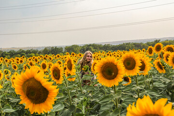 face of  young blond woman among sunflowers in  field, smiling, satisfied, view from afar, large...