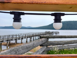 soft, warm light from decorative lamps hangs above wooden pier extending into calm lake. still...