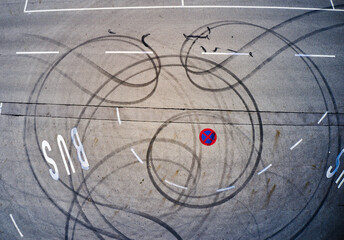 Aerial view of dark tire tracks creating swirling patterns around a bus stop sign on the asphalt, Marktoberdorf, Bavaria, Germany.