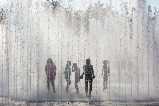 Children playing among the stream of water pouring from the park's floor fountain in the summer
