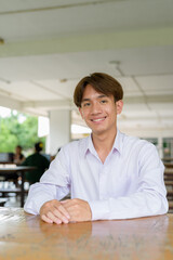 Non binary university student sitting and smiling in college campus