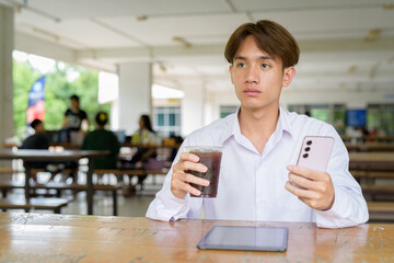 Non binary university student sitting in college campus using phone