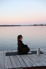 Woman practicing yoga on a wooden pier by the water at sunrise. Peaceful atmosphere, healthy...