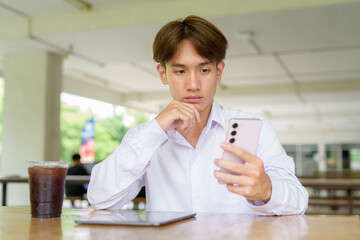 Non binary university student sitting in college campus using phone
