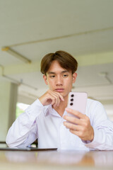 Non binary university student sitting in college campus using phone