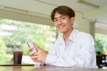 Non binary university student sitting in college campus using phone