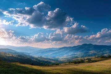 Naklejka premium Grassy hills meet blue mountains and cloudy sky with sunlight piercing through clouds