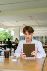 Non binary university student sitting in college campus using tablet computer
