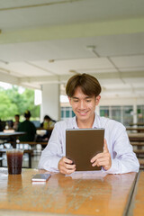 Non binary university student sitting in college campus using tablet computer