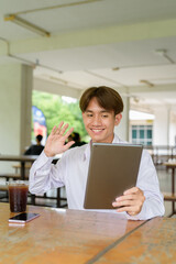 Non binary university student sitting in college campus using tablet computer