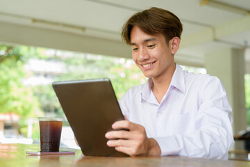 Non binary university student sitting in college campus using tablet computer