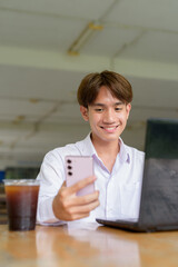 Non binary university student sitting in college campus using laptop computer and phone