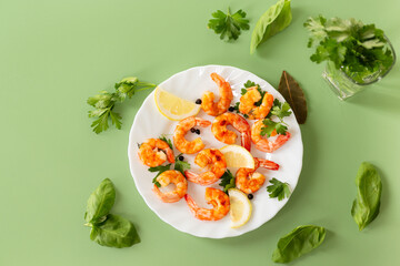 Delicious sea shrimps with lemon in a plate isolated on green
