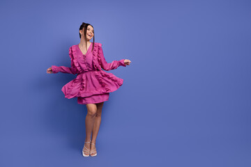 Elegant young woman dancing in a vibrant pink dress with ruffles against a rich purple background,...