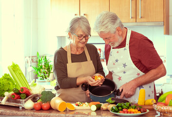 Smiling senior couple working together in the home kitchen preparing vegetables for a healthy soup....