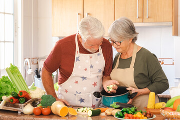 Smiling senior couple working together in the home kitchen preparing vegetables for a healthy soup....