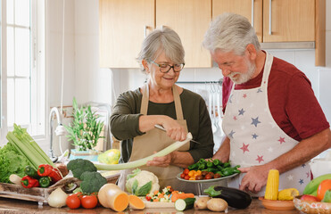 Smiling senior couple working together in the home kitchen preparing vegetables for a healthy soup....