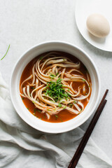 Overhead view of spicy noodle soup in a white bowl, top view of noodles in a spicy broth with scallions