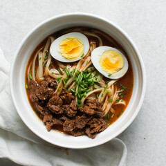 Overhead view of spicy noodle soup with eggs in a white bowl, top view of noodles eggs in a spicy broth with scallions