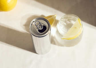 a cold clear glass of lemonade on the table illuminated by a bright light and a metal can of soda